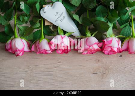 Cuore bianco in porcellana e iscrizione sullo sfondo in legno con fiori rosa. Segno di matrimonio o d'amore. Posiziona per testo. Foto Stock