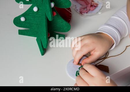 La mano del bambino fa pupazzo di neve e albero di natale con ago, filo per il biglietto di auguri di natale. Concetto di hobby. Fatto a mano. Foto Stock