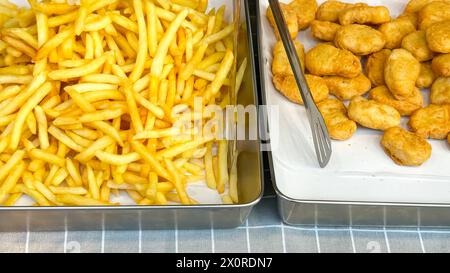 Patatine fritte croccanti e pepite di pollo dorate sono esposte in vassoi di metallo, pronti per un servizio veloce in una bancarella di Street food con un'atmosfera informale e da asporto Foto Stock