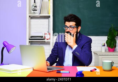 Professione, apprendimento, istruzione e concetto di conoscenza. Lavoro da insegnante. Un insegnante universitario sorpreso lavora su un computer portatile in classe. Scuola superiore Foto Stock