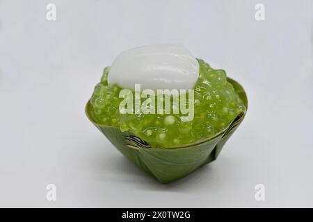 Primo piano di un dessert tailandese Khanom Tako "capovolto", con condimento verde al sago di palma e un pizzico di crema di cocco Foto Stock