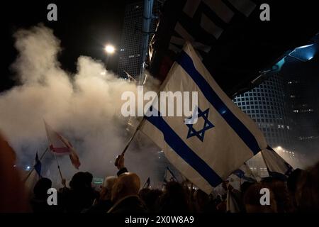 Tel Aviv, Israele. 16 marzo 2024. I manifestanti tengono le bandiere israeliane sotto il ponte pedonale dell'Azrieli Center, mentre intorno a loro sparge fumo proveniente da un falò spento. Due proteste si fondono al di fuori del quartier generale militare di Kirya a Tel Aviv. Uno chiedeva elezioni immediate per spodestare Netanyahu, l'altro chiedeva il rilascio degli ostaggi ancora detenuti da Hamas. Credito: SOPA Images Limited/Alamy Live News Foto Stock