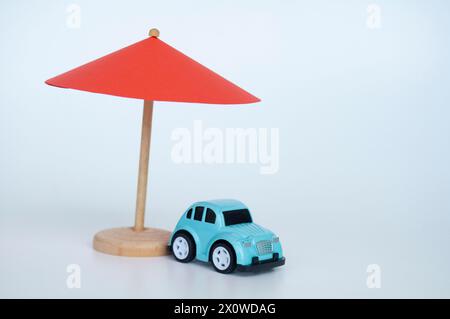 Ombrello giocattolo rosso e macchinetta giocattolo blu su sfondo bianco. Foto Stock