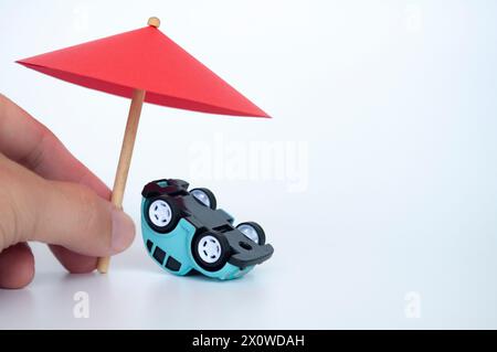 Ombrello giocattolo rosso e auto capovolta su sfondo bianco. Concetto di assicurazione auto. Foto Stock