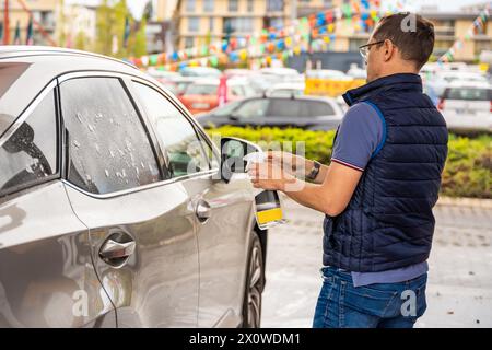 Il giovane applica il liquido per pulire i finestrini dell'auto in autolavaggio self-service Foto Stock