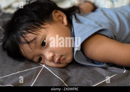 Il bambino si stese sul letto e si addormentò, pisolava o era triste. Foto Stock