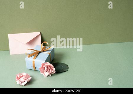 Confezione regalo blu e busta con rosa rosa sul tavolo verde. sfondo parete cachi. concetto di celebrazione del compleanno Foto Stock