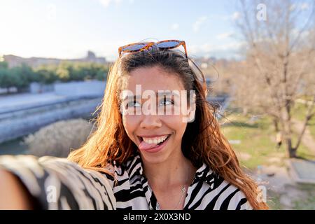 selfie di una donna latina che fa una faccia divertente, che le rimbalza la lingua e incrocia gli occhi. ritratto di una giovane donna Foto Stock