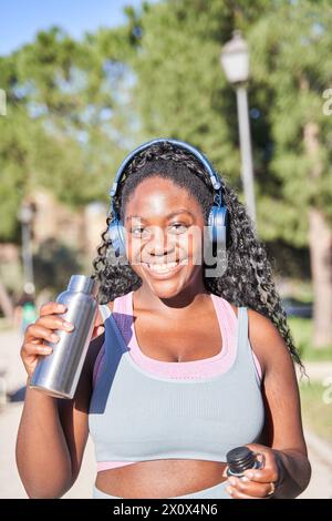 Donna afroamericana che beve acqua durante una pausa in allenamento all'aperto. Foto Stock