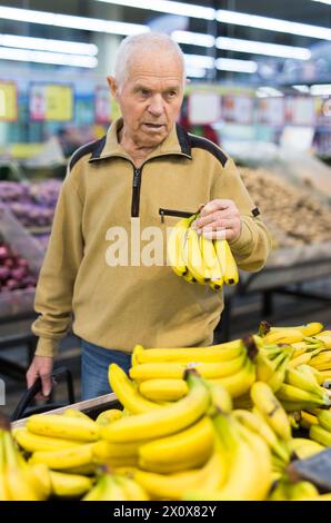 Senor man pensionato che compra banane al supermercato Foto Stock