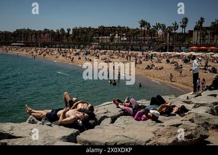 Barcellona, Spagna. 14 aprile 2024. 14 aprile 2024, Barcellona, Spagna: In questa calda e soleggiata domenica di aprile, le persone prendono il sole e si rilassano su una frangiflutti sulla spiaggia di Barceloneta a Barcellona. Crediti: Jordi Boixareu/Alamy Live News Foto Stock