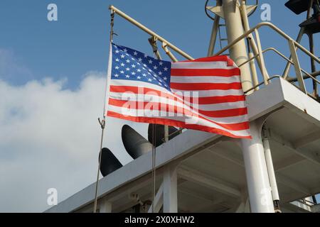Bandiera americana sul vento appeso all'albero di navigazione vicino ai tubi di scarico dell'imbuto sulla nave mercantile. Foto Stock