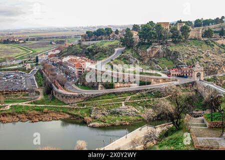 Valle con colline rocciose con erba verde, edifici, strade rurali per veicoli e fiume Tago, parte di Alcazar in uno sfondo nebbioso e sfocato, visto da vi Foto Stock