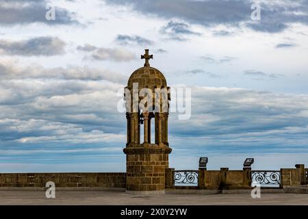 Campanile in pietra in stile neogotico della chiesa Sagrat Cor sulla cima del monte Tibidabo, croce su piccola cupola, spianata superiore, giornata nuvolosa con cielo azzurro Foto Stock