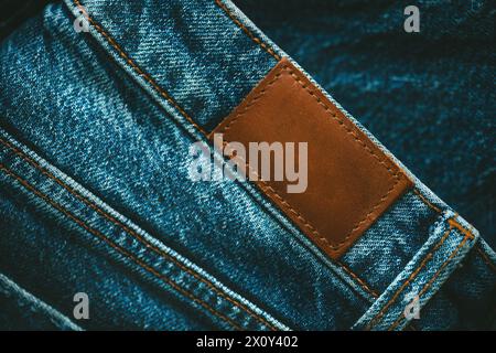 Etichetta vuota in pelle marrone con jeans vuoti cucita su jeans blu. Stile, denim e stile. Foto Stock