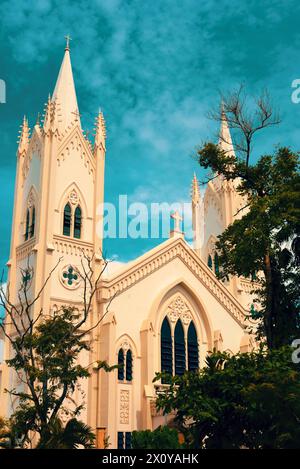 Una splendida chiesa storica, esposta contro un vivace cielo blu, la sua complessa architettura illuminata dal caldo bagliore del sole e dai verdi lussureggianti. Foto Stock