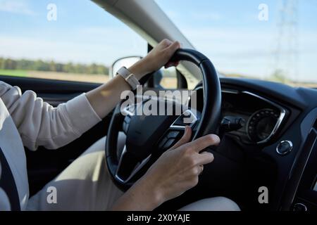 Vista interna di una donna che guida un'auto su una strada di campagna. Conducenti femminili mani sul volante Foto Stock