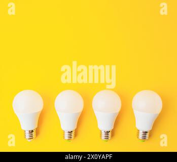 Quattro lampadine bianche sono disposte su sfondo giallo. Le lampadine hanno tutte le stesse dimensioni e la stessa forma e sono distanziate uniformemente. Concetto di unif Foto Stock