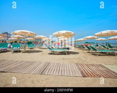 Passerella sulla spiaggia lungo una fila di ombrelloni colorati e lettini che conducono al mare in una soleggiata giornata estiva sulla riva del Mare Adriatico, in Italia. Foto Stock