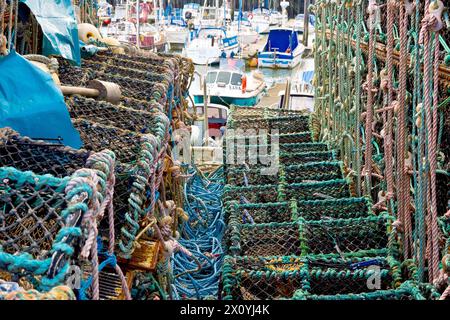 Primo piano di vasi di aragosta, granchi o aragosta accumulati sulla banchina del porto di Arbroath durante l'inverno, con le barche nel molo interno in lontananza. Foto Stock