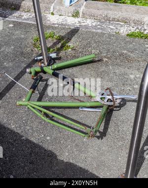 Telaio della bicicletta verde incatenato a una barra metallica sul terreno. La moto è danneggiata con la catena appesa al telaio Foto Stock