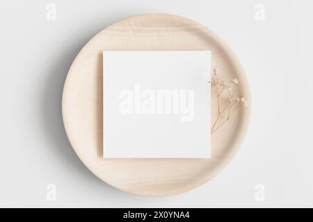 Mockup di tessera quadrata d'invito su un piatto di legno con una gitsofila. Foto Stock