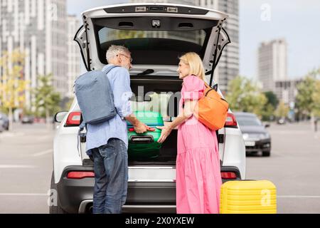 Coppia di anziani che stiva borse nel bagagliaio dell'auto Foto Stock