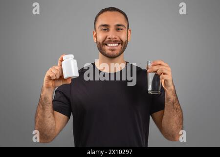 Uomo sorridente che tiene in mano una bottiglia di pillola e dell'acqua Foto Stock