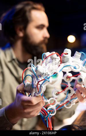 Concentratevi sulle cuffie EEG utilizzate dai professionisti IT in background sfocato per comunicare con l'intelligenza artificiale sul computer. Primo piano di un dispositivo high-tech utilizzato dallo sviluppatore di software Foto Stock