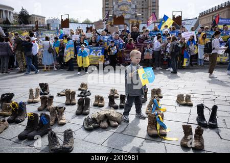 Kiev, Ucraina. 13 aprile 2024. Un ragazzo con una bandiera Ucraina si trova accanto a stivali militari posti da parenti e amici di soldati ucraini scomparsi durante una dimostrazione. Nelle battaglie per la città di Bakhmut contro la formazione militare russa Wagner Group organizzò una manifestazione che invitò le autorità a localizzare e restituire i soldati ucraini scomparsi in azione, nonché i prigionieri di guerra dalla prigionia russa. (Credit Image: © Oleksii Chumachenko/SOPA Images via ZUMA Press Wire) SOLO PER USO EDITORIALE! Non per USO commerciale! Foto Stock