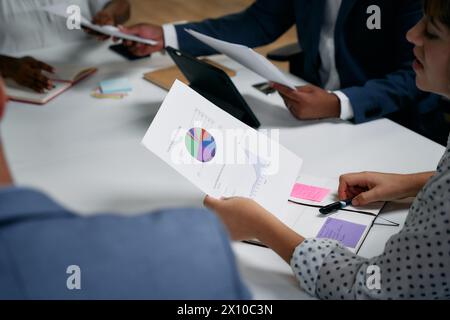 Quattro adulti multirazziali che esaminano il documento con un grafico durante una riunione d'affari in ufficio Foto Stock