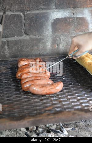 Una persona sta cucinando hot dog su una griglia. Gli hot dog sono su una griglia metallica e vengono cotti su una fiamma libera Foto Stock