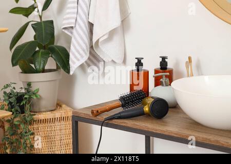 Spazzola rotonda con asciugacapelli sul tavolo in bagno, primo piano Foto Stock