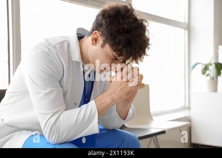 Stress sesso maschile medico stagista seduto in clinica Foto Stock