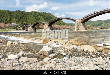 Un ponte attraversa un fiume con una costa rocciosa. Il ponte è circondato da alberi e da un piccolo villaggio Foto Stock