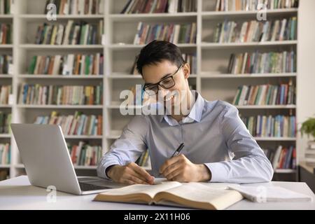 Sorridente intelligente studente indiano fa esercizio in copybook Foto Stock