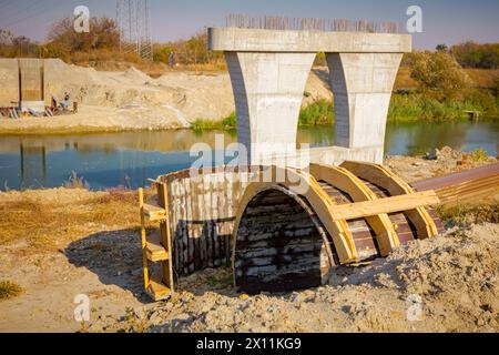 Stampi ad arco in legno per il ponte, grande e moderno pilastro in cemento grigio nelle fondamenta circondato da pali di metallo. Il palo rinforzato in fase di costruzione è trasversale Foto Stock