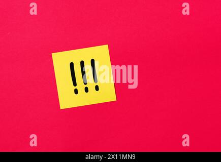 Tre punti esclamativi scritti a mano su una carta adesiva gialla fissata su una lavagna rossa. Concetto di avviso importante. Foto Stock