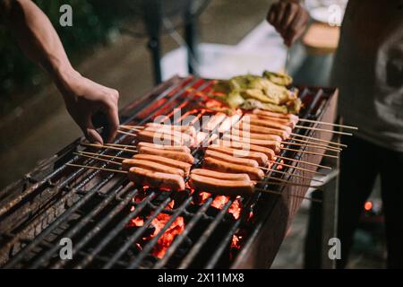 Le salsicce grigliate spiedate sugli spiedini sono preparate per essere grigliate su una griglia utilizzando carbone Foto Stock