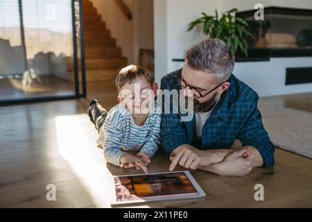 Padre che mostra al figlio un sistema di casa intelligente, che regola le funzioni domestiche, l'illuminazione, le telecamere di sicurezza, le serrature delle portiere e le impostazioni del termostato o del riscaldamento intelligenti Foto Stock