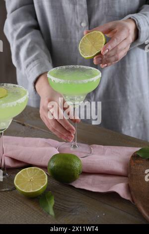 Donna che spreme il succo di lime nel bicchiere con un delizioso cocktail Margarita al tavolo di legno, primo piano Foto Stock