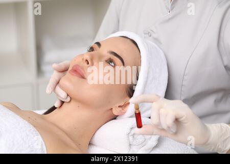 Cosmetologo professionista che tiene in mano una fiala per la cura della pelle mentre lavora con il cliente in clinica, primo piano Foto Stock