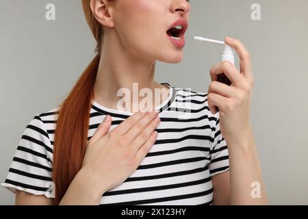 Giovane donna che usa spray per la gola su sfondo grigio, primo piano Foto Stock