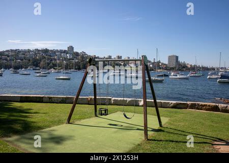 Parco giochi per bambini Sydney, Australia, con due altalene sulla spiaggia Forty Baskets e riserva con vista sugli yacht nel porto fino al sobborgo di Manly Beach Foto Stock