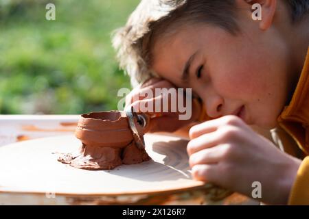 Ragazzo che taglia un pezzo di argilla per fare la ceramica sulla ruota del vasaio Foto Stock