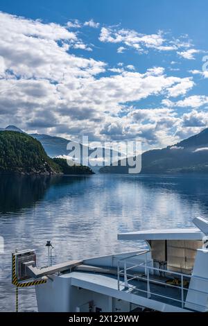 Un traghetto naviga attraverso le calme acque del fiordo, con montagne e nuvole bianche in una giornata estiva di sole a Stangvikfjord in Norvegia Foto Stock