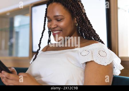 Una giovane donna birazziale con i capelli intrecciati che sorride al telefono Foto Stock