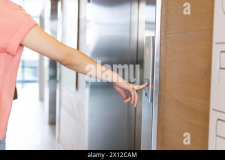 Una giovane donna asiatica sta premendo il pulsante dell'ascensore in un moderno ufficio d'affari Foto Stock