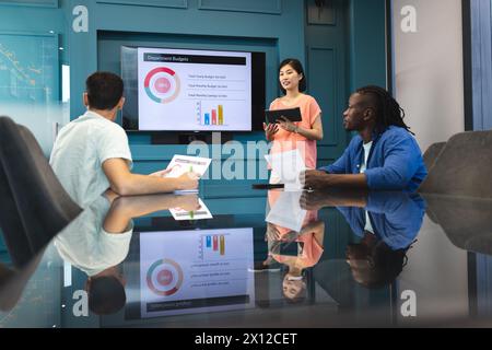 Donna asiatica che presenta a uomini birazziali e afroamericani in un moderno ufficio d'affari Foto Stock