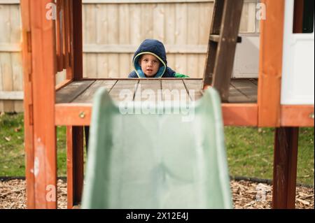 Un ragazzino che si arrampica sul parco giochi nel cortile per scendere lo scivolo Foto Stock